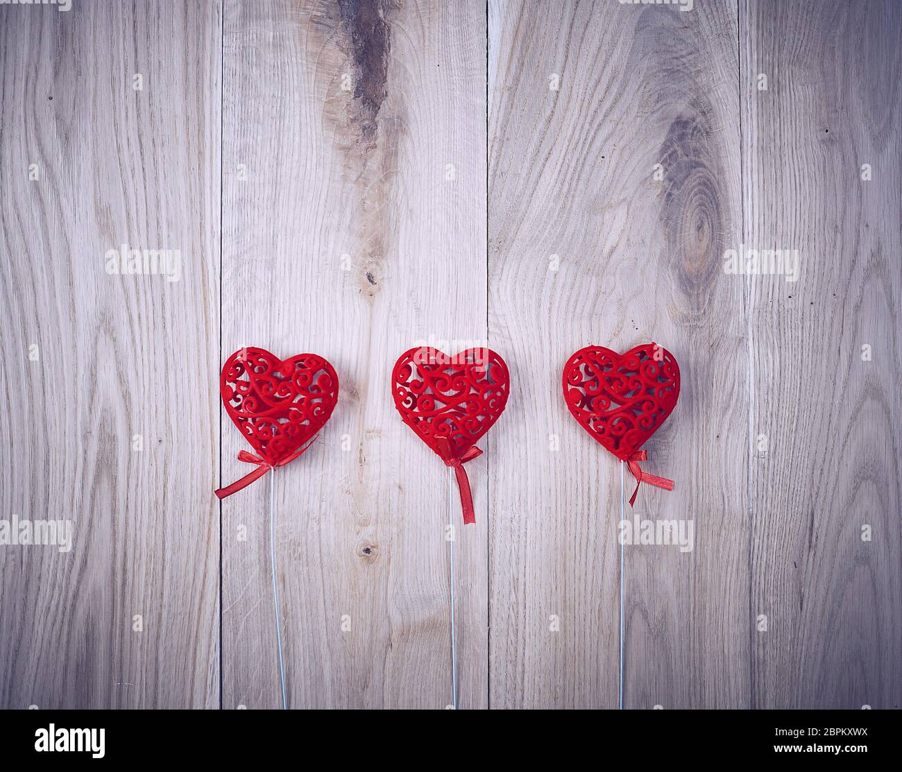 three red carved hearts on a stick on a wooden background,  copy space Stock Photo