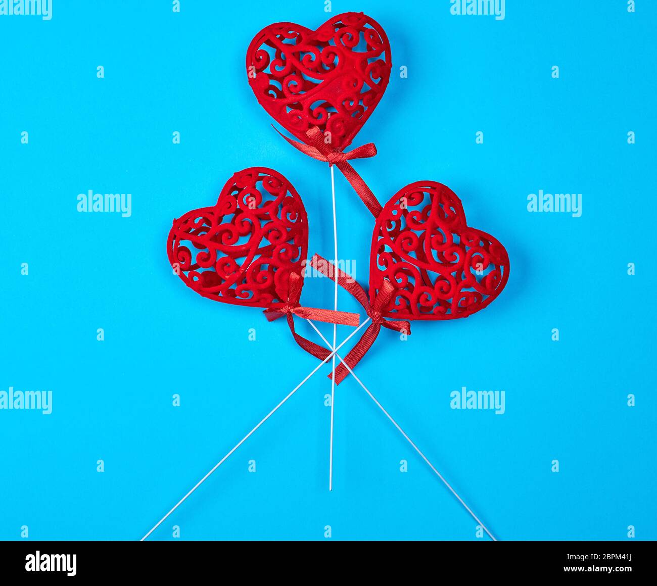 three red carved hearts on a stick on a blue background Stock Photo