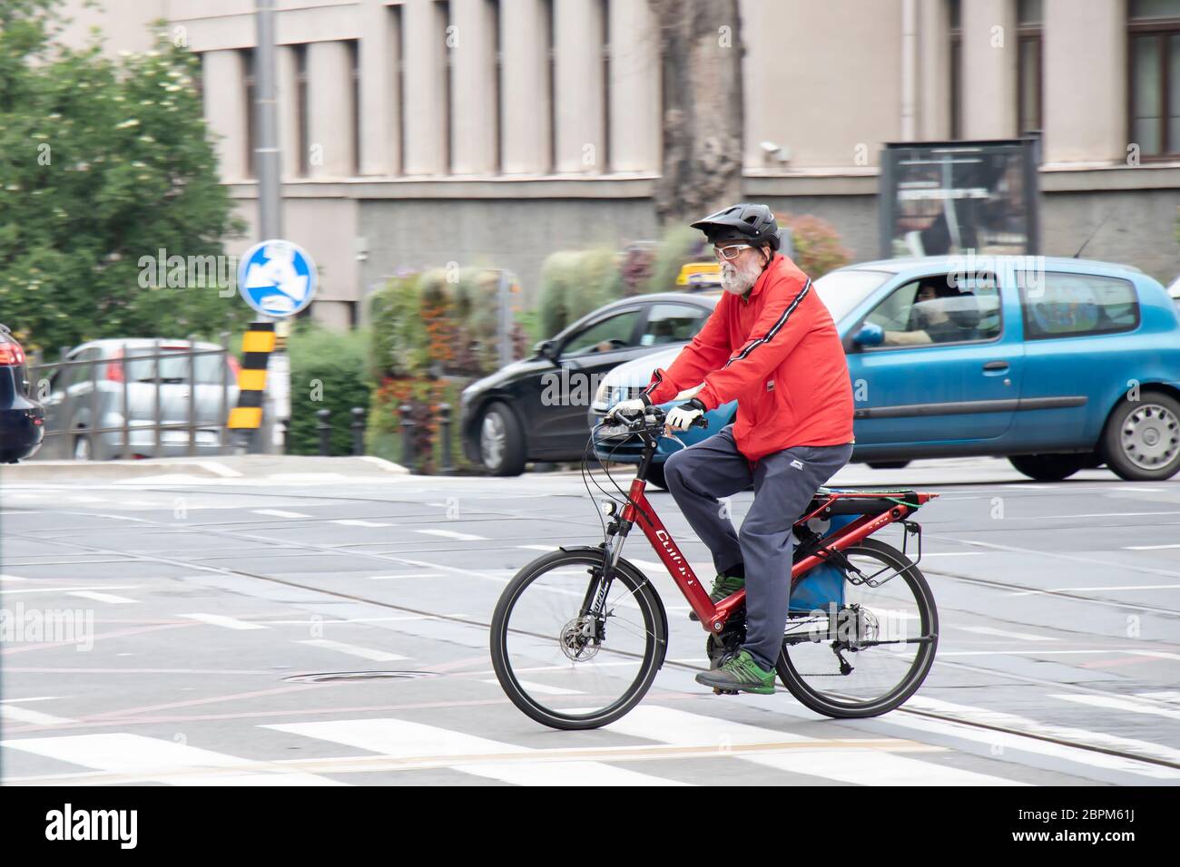 Belgrade, Serbia - May 15, 2020: Elder man with gray beard riding a red bike in city street traffic Stock Photo