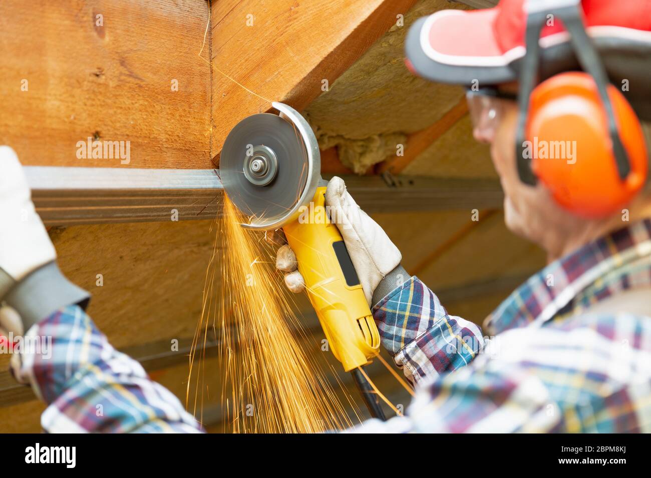 Man fixing metal frame using angle grinder on attic ceiling covered with rock wool Stock Photo