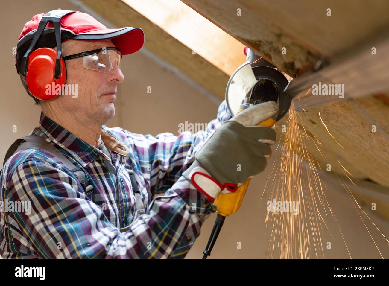 Man fixing metal frame using angle grinder on attic ceiling covered with rock wool Stock Photo