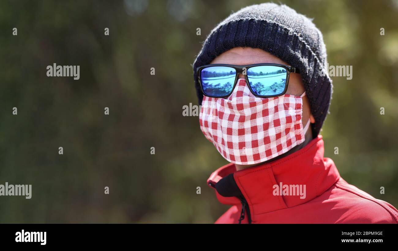 Man wearing beanie hat, blue shiny sunglasses and white red cotton home  made nose mouth face virus mask, closeup detail portrait, blurred park  trees b Stock Photo - Alamy