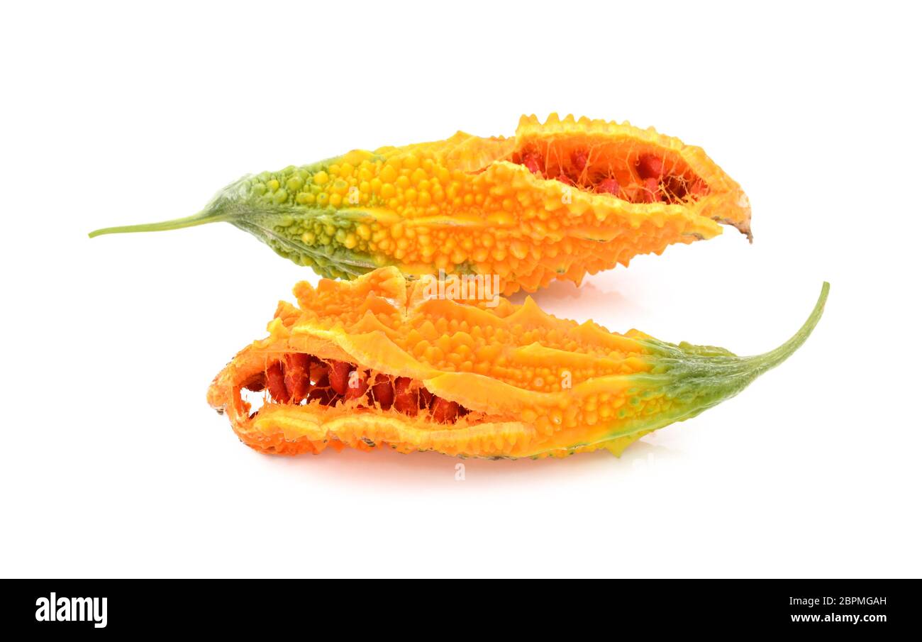 Two overripe bitter melon fruits with orange and green skin, splitting open to show red seeds inside, isolated on a white background Stock Photo