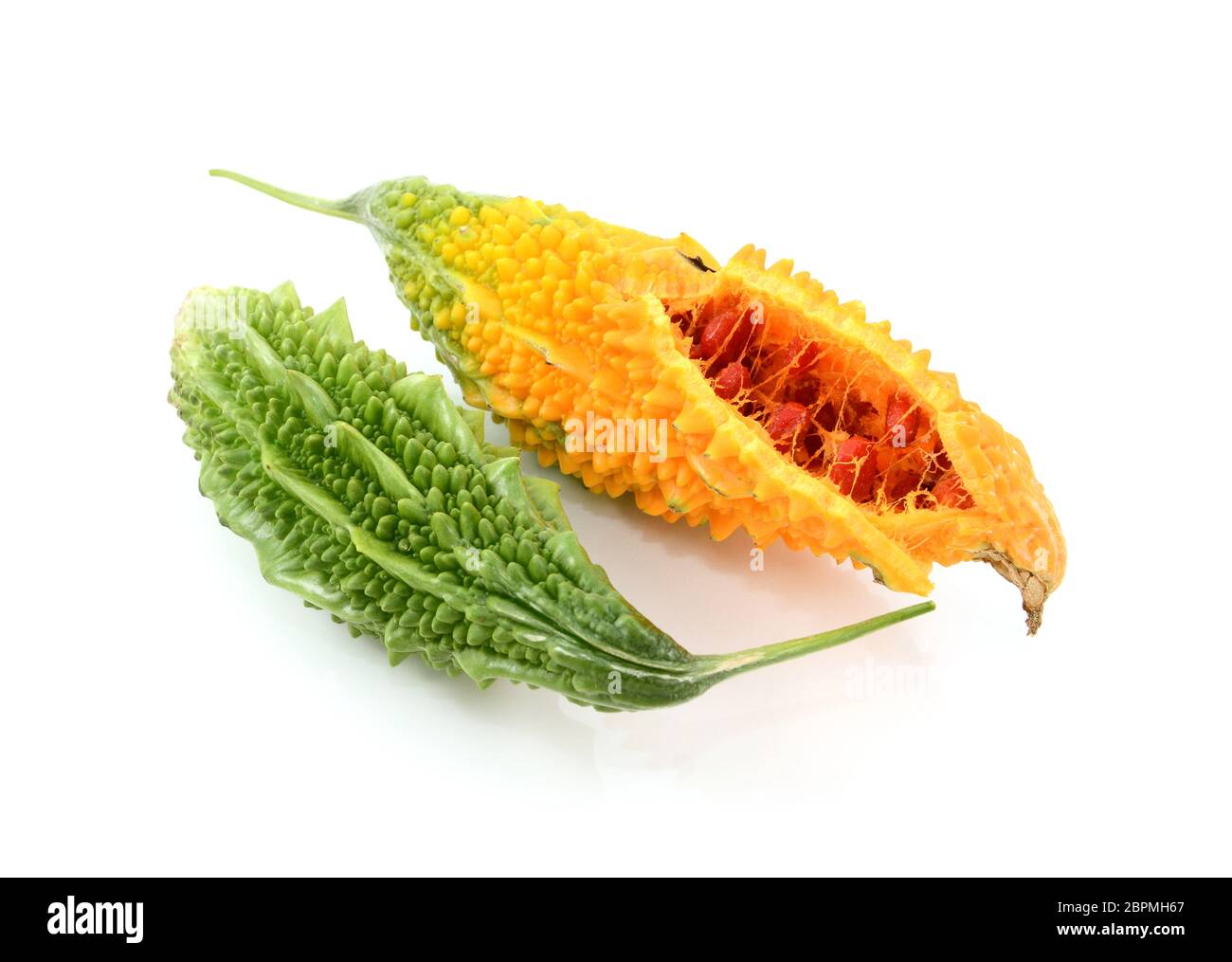 Two ripe bitter melons green and whole, and orange, split open with