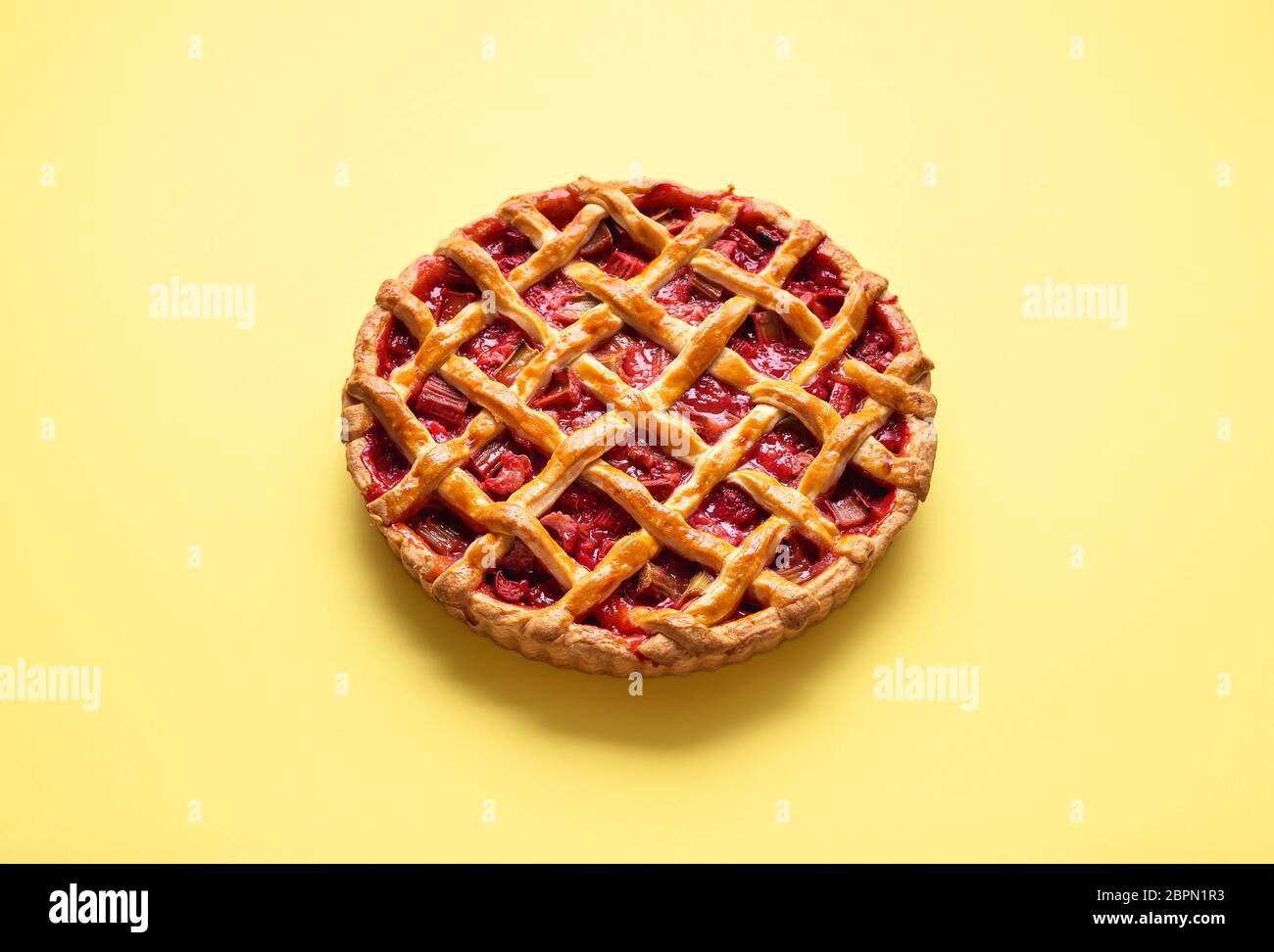 Strawberryrhubarb pie with a lattice crust on a yellow seamless