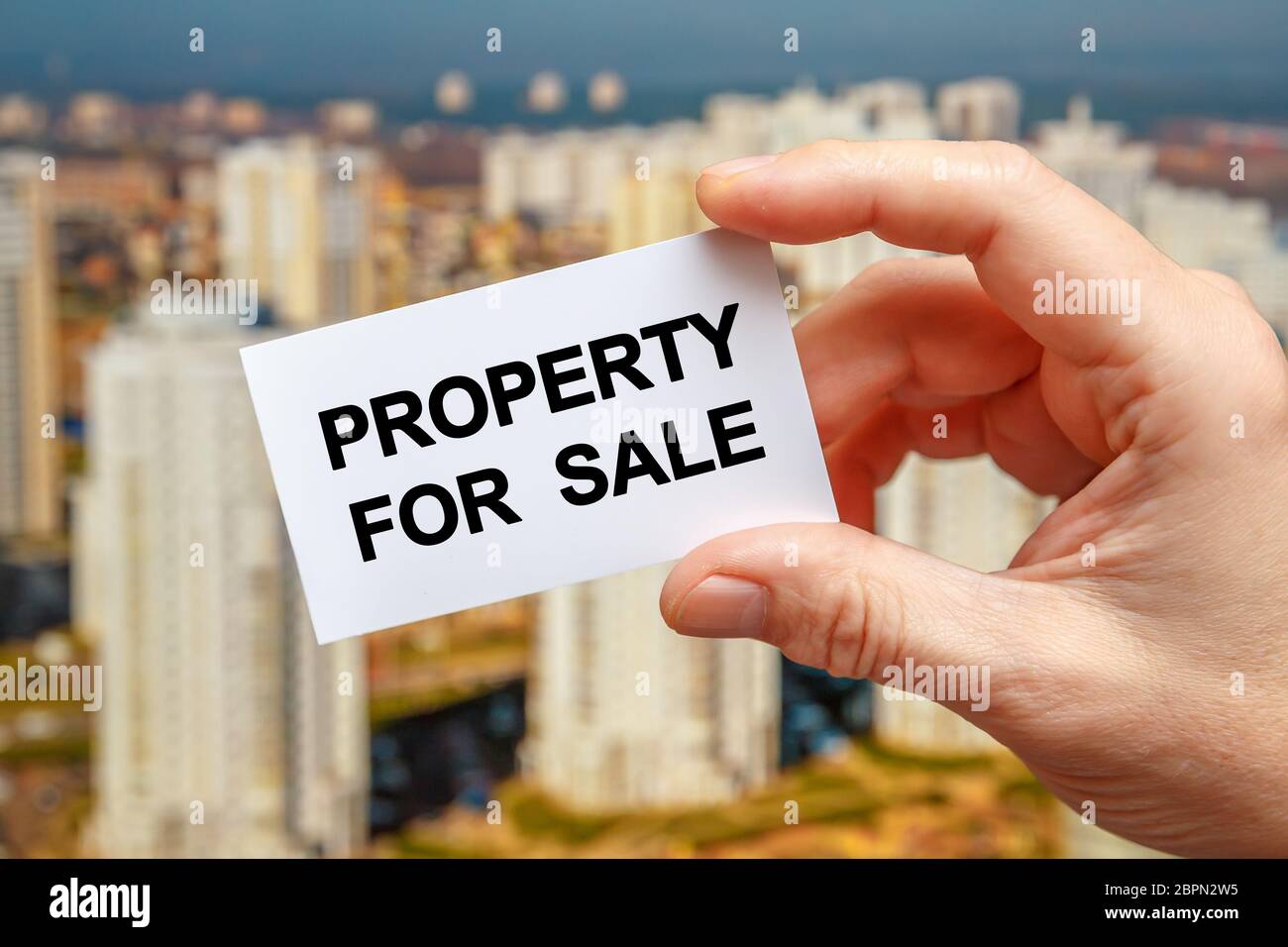 Property for sale - the inscription on the card that a person holds against the background of the city. Property value concept Stock Photo