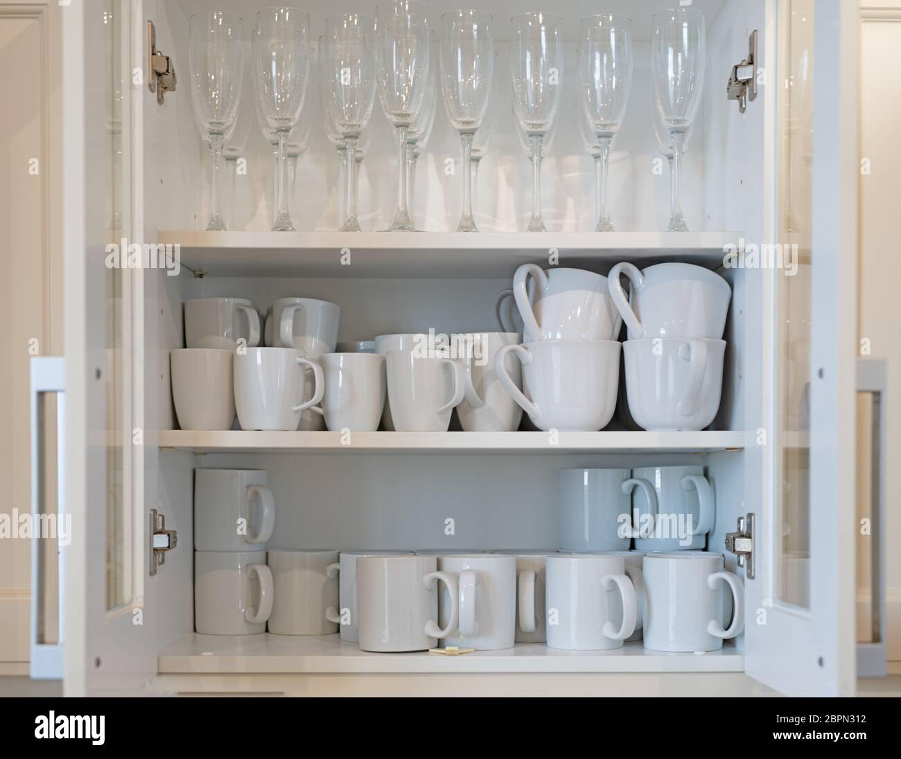Cupboard full of white mugs and champagne glasses Stock Photo Alamy