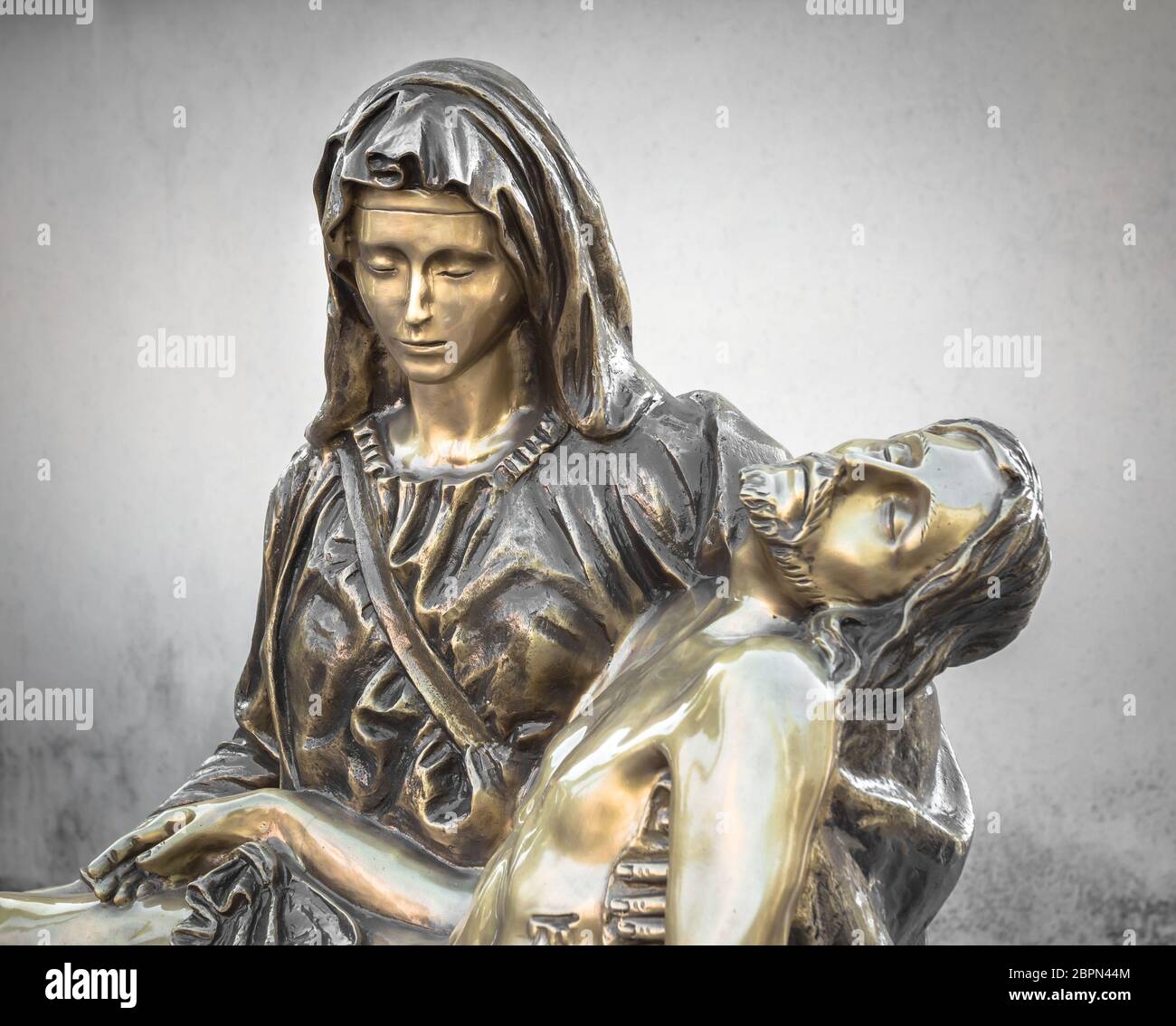 Bronze Statue of dead Jesus Christ down from the cross, being embraced by the Virgin Mary. On background a gray rough wall. It can be used for concept Stock Photo