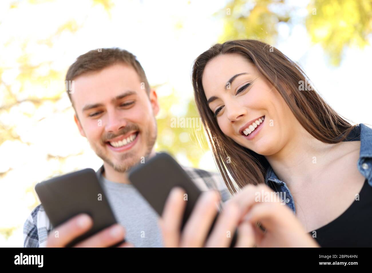 Portrait of a happy couple using their smart phones walking in a park Stock Photo