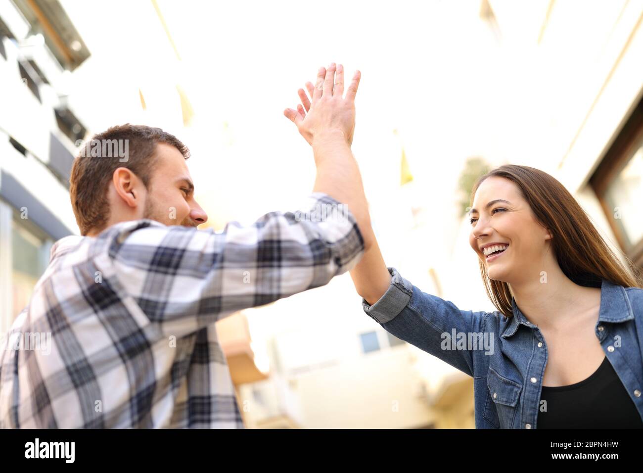 Two happy friends giving high five standing in a city street Stock ...