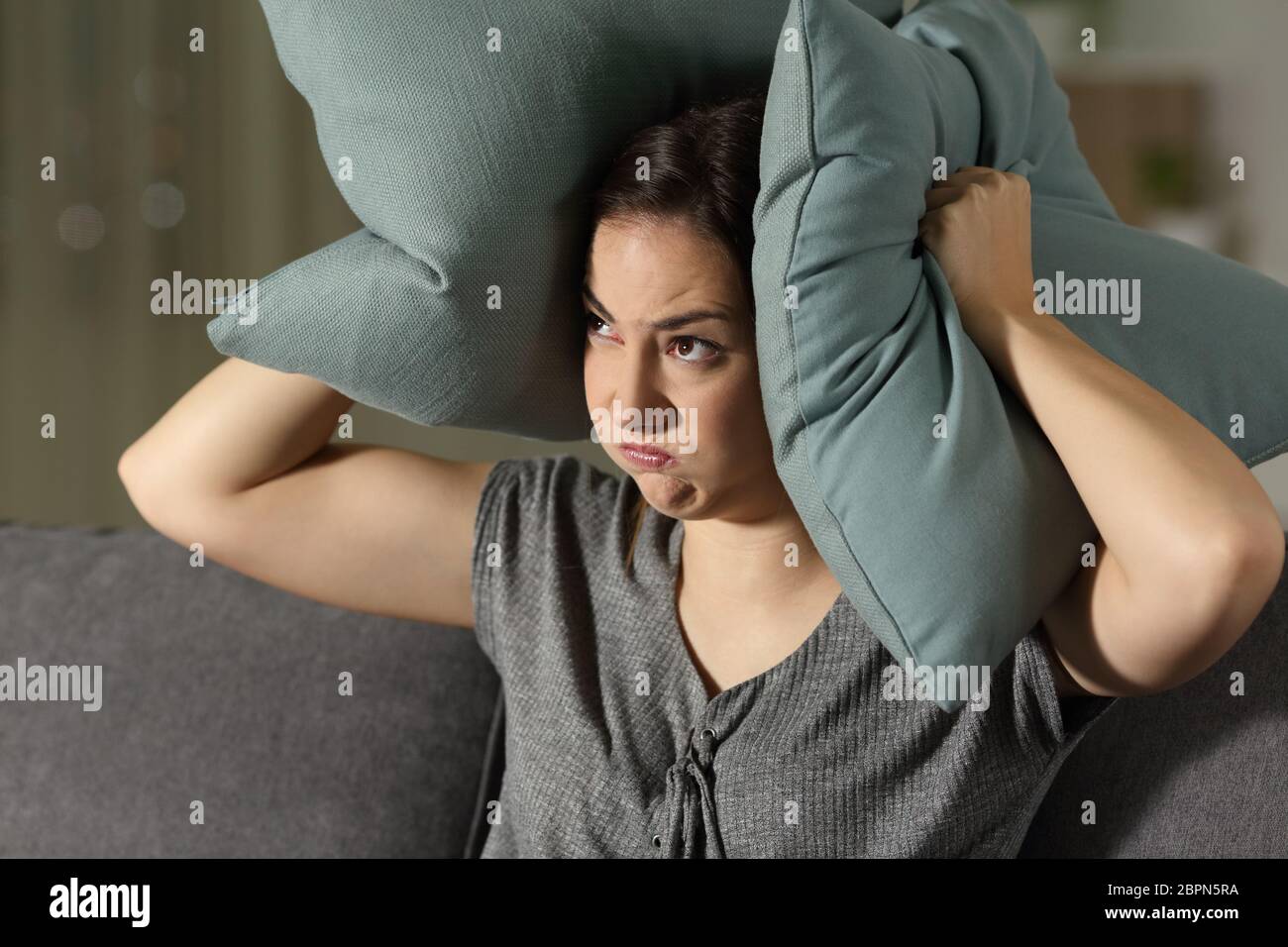 Angry woman suffering neighbour noise sitting on a couch in the living