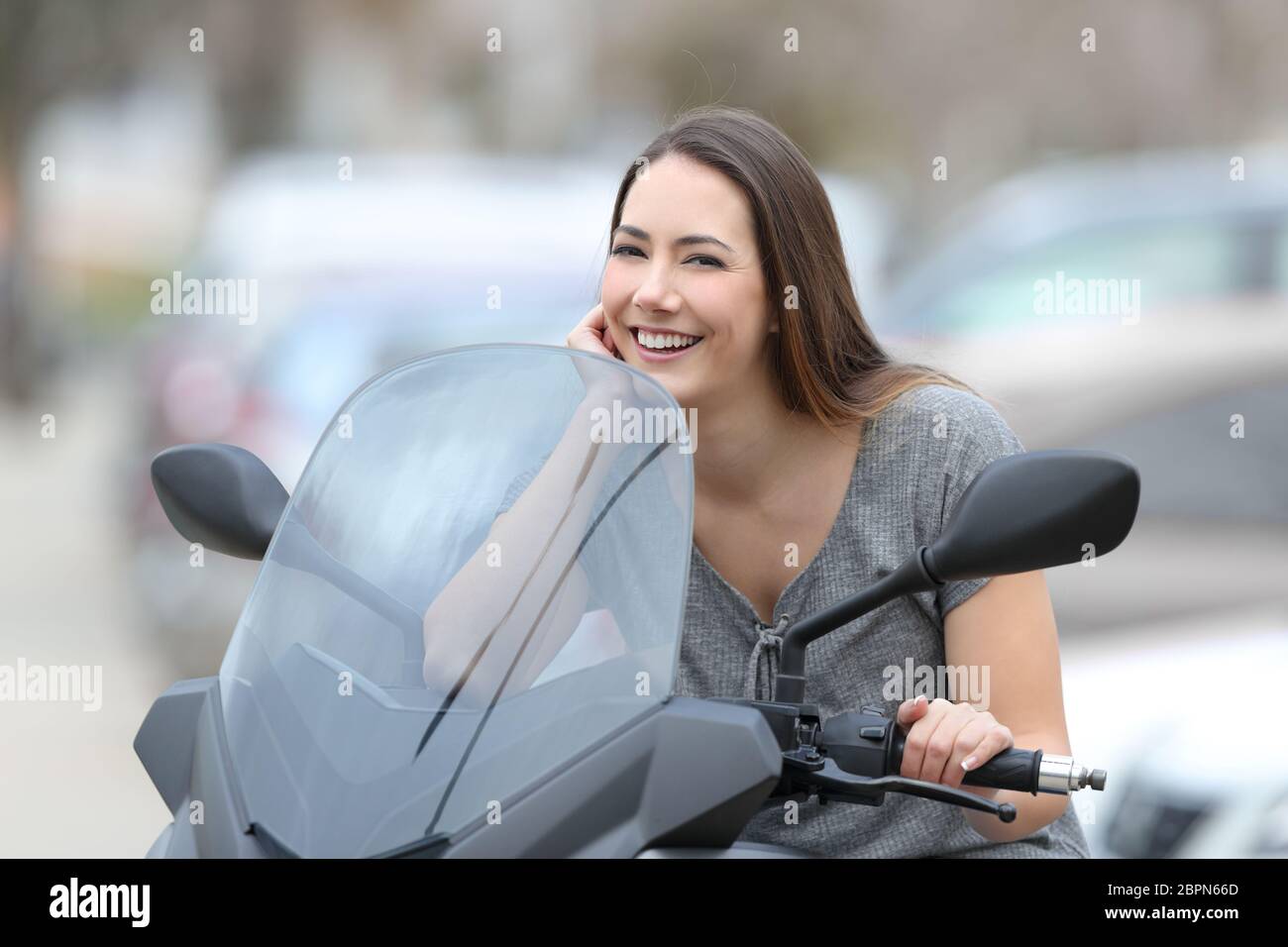 Portrait of a happy biker posing looking at camera on a motorbike on the street Stock Photo
