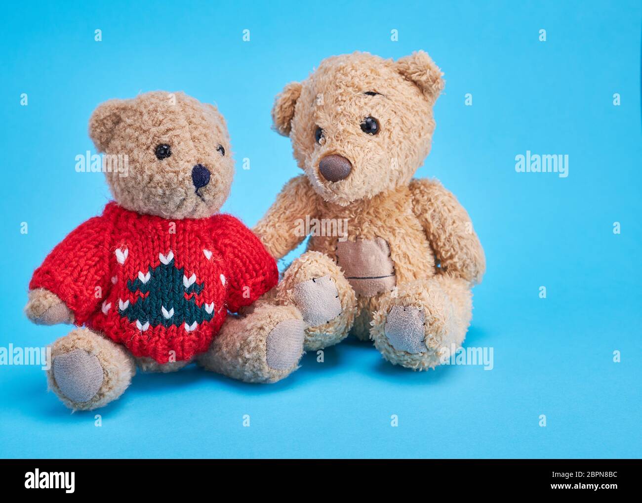 two teddy bears are sitting side by side on a blue background Stock Photo