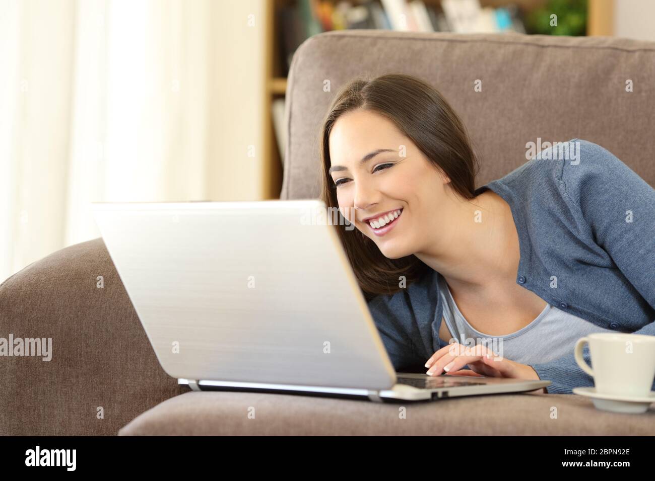 Woman using a laptop lying on a couch in the living room at home Stock ...