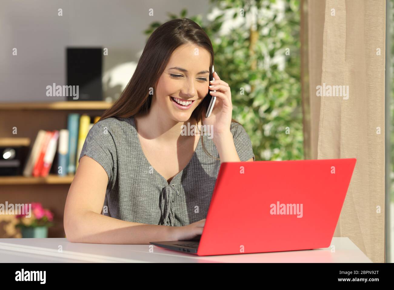 Attractive housewife using a red laptop and calling to the assistance ...