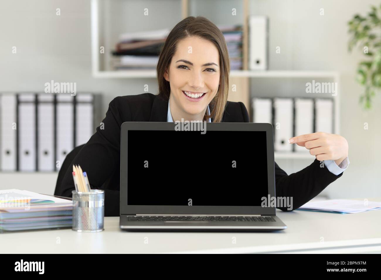 Front view portrait of a happy office worker pointing at a laptop screen mockup Stock Photo