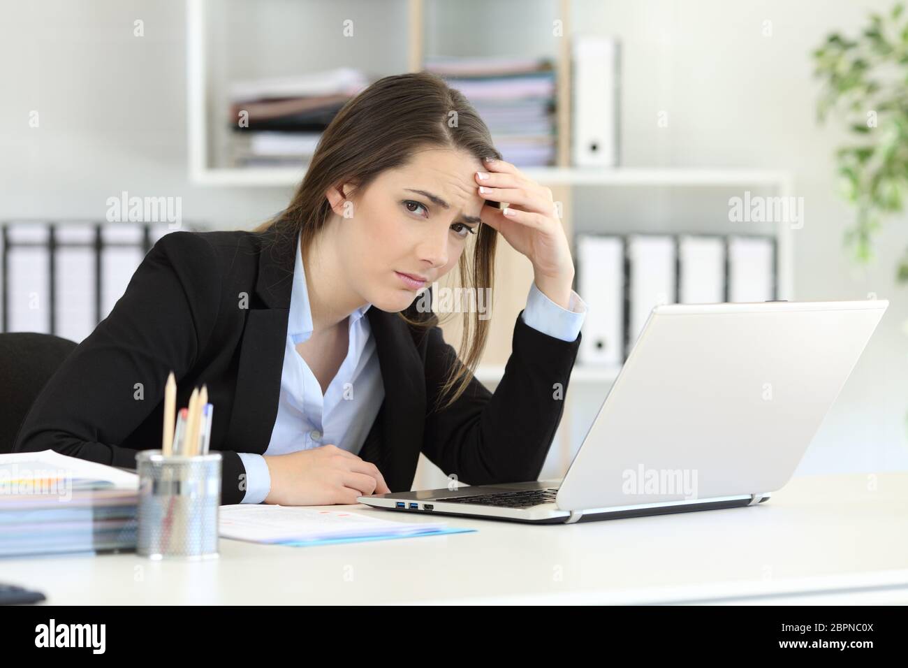 Worried office worker looking at camera sitting in a desktop Stock Photo