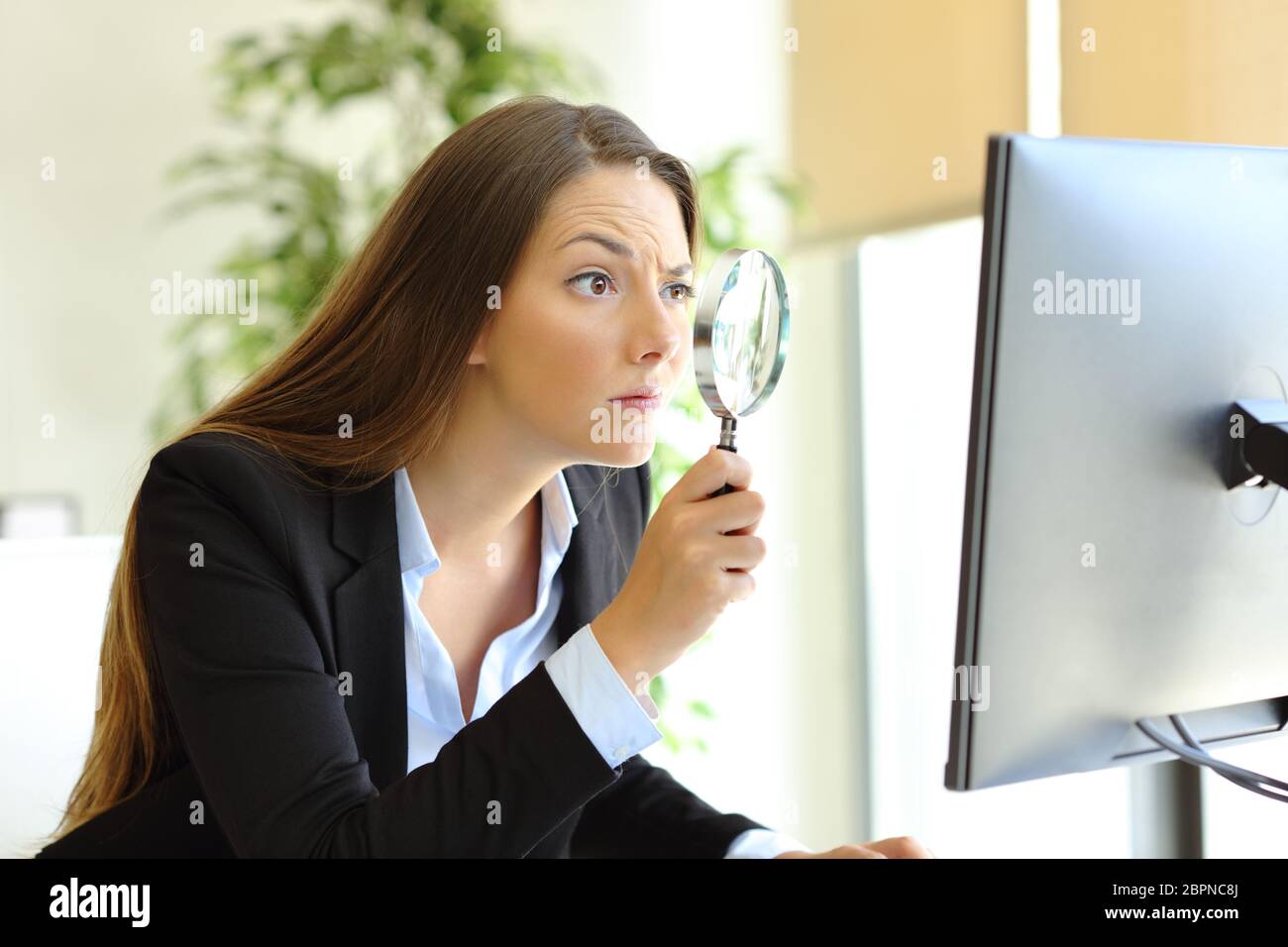 Suspicious office worker checking online content on computer using a magnifying glass Stock Photo