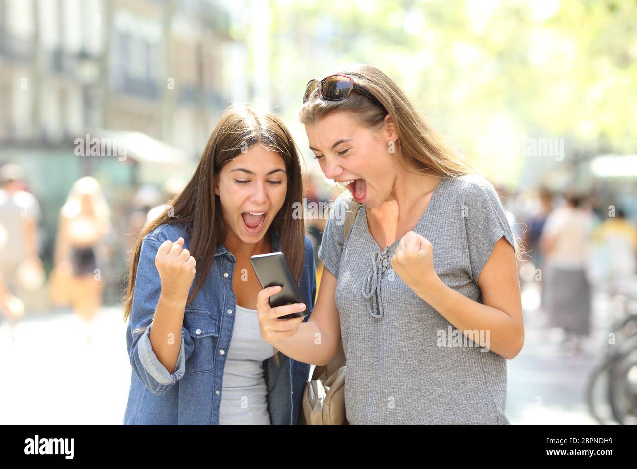 Two excited winners watching online content in a smart phone in the street Stock Photo