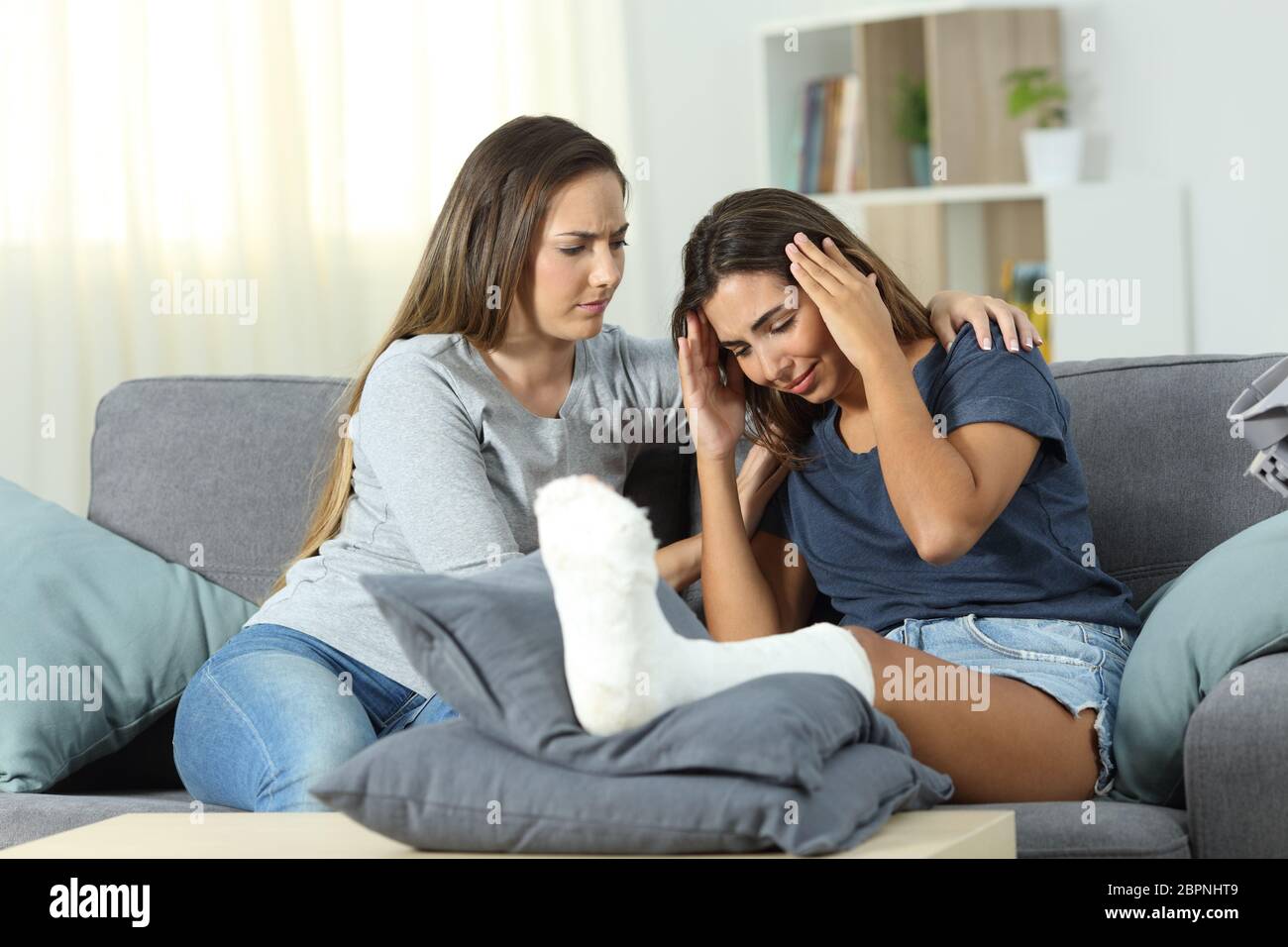 Sad disabled woman and friend comforting her sitting on a couch in the living room at home Stock Photo