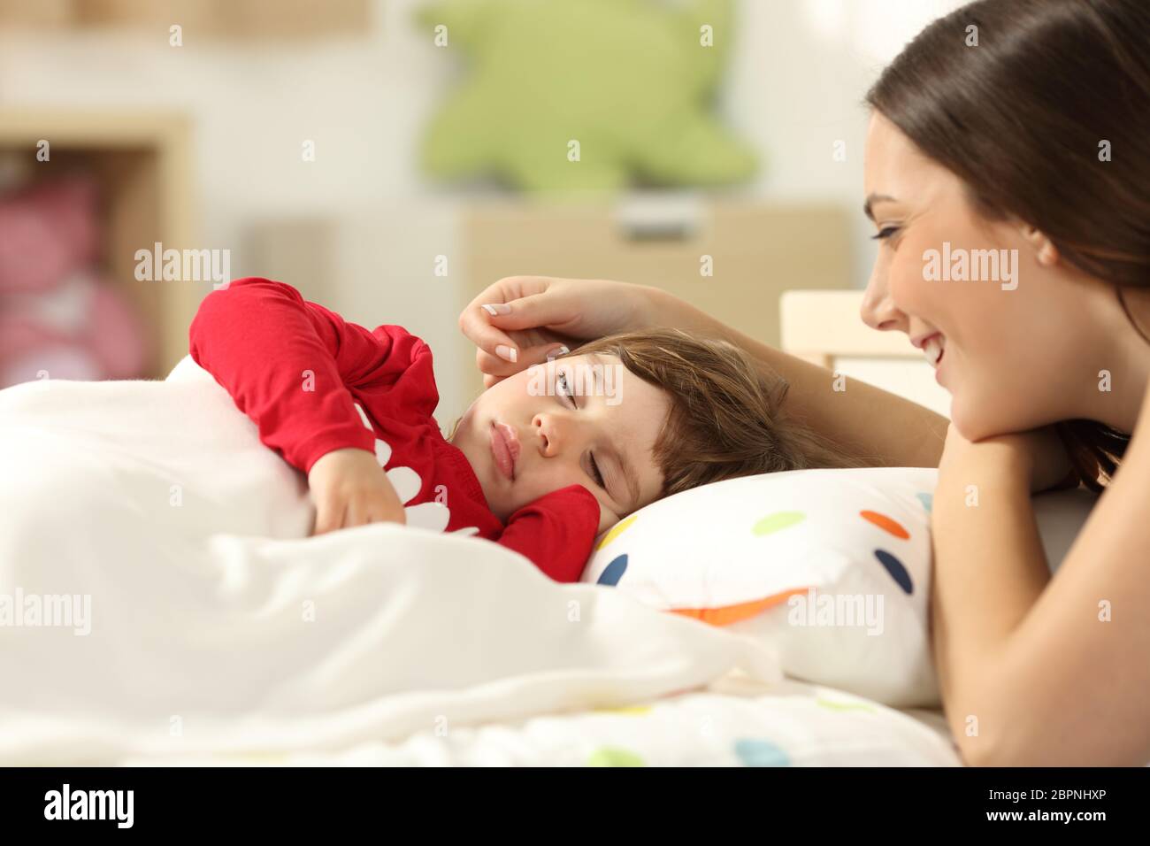 Affectionate mother looking at her toddler girl sleeping in a bed in her room at home Stock Photo