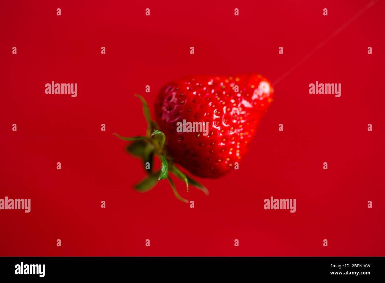 one red ripe strawberry on a red background Stock Photo - Alamy
