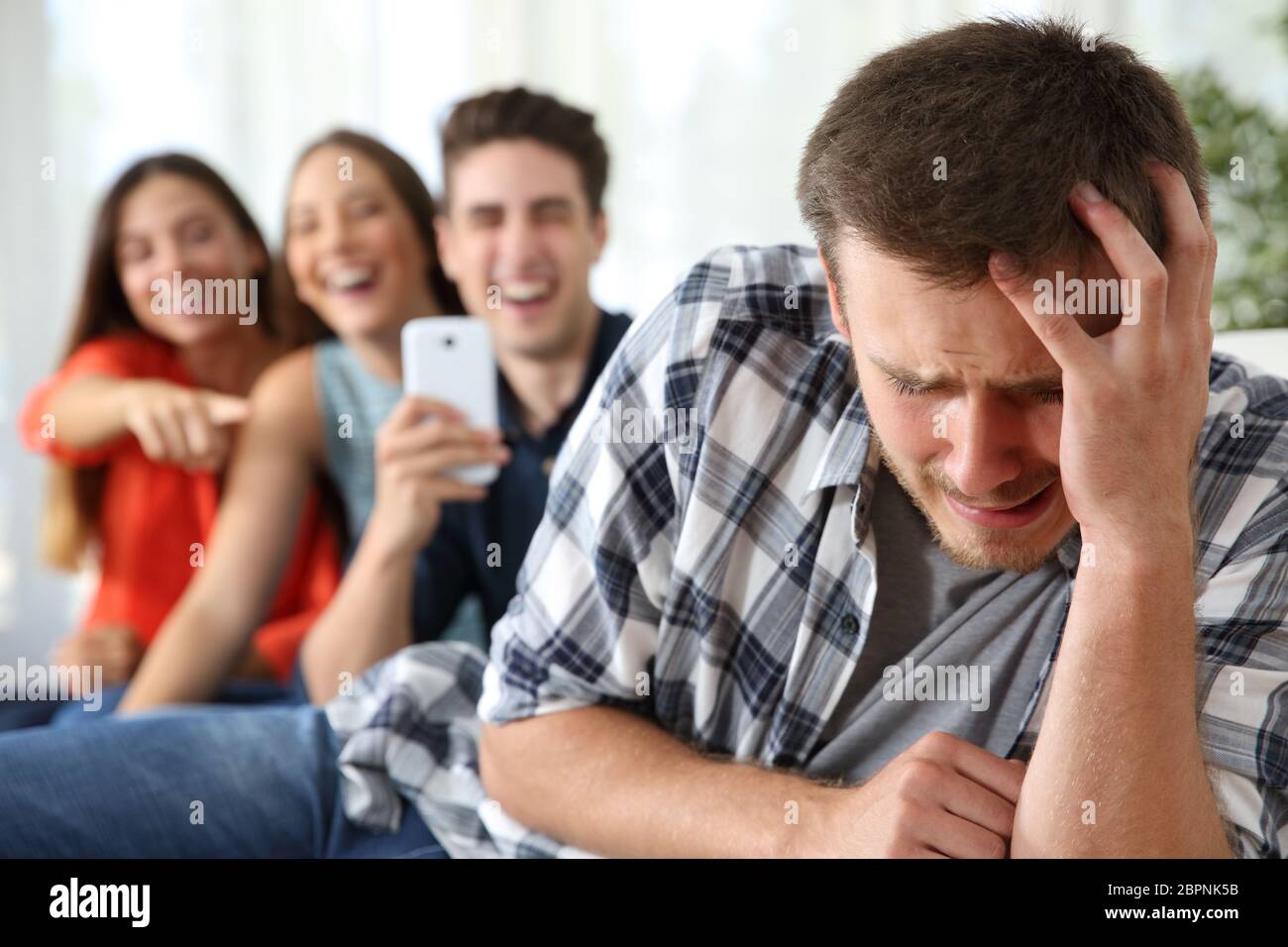 Friends bullying to a sad boy and taking photos with a smartphone for the social network Stock Photo