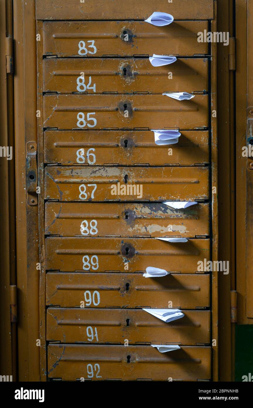 Old mailboxes in the entrance hall of a residential house filled with white paper flyers. Mass mailing concept Stock Photo