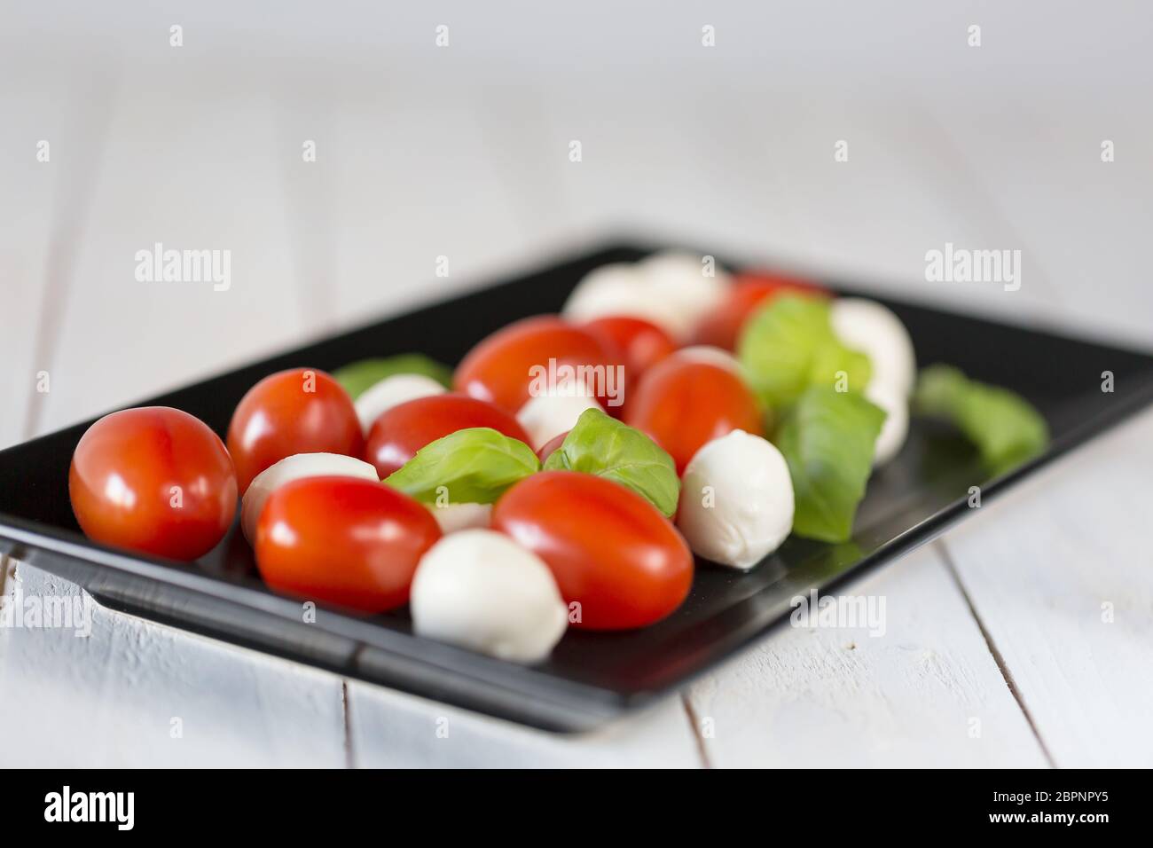 Fresh mozzarella cheese balls with cherry tomatoes and green basil isolated on white background