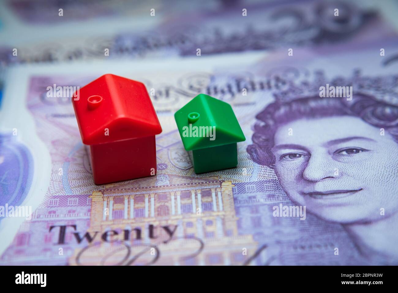 The red toy house placed on top of 20 British pound notes. Macro photo. Concept image for UK House Price Index, first home, mortgage, real estate or h Stock Photo