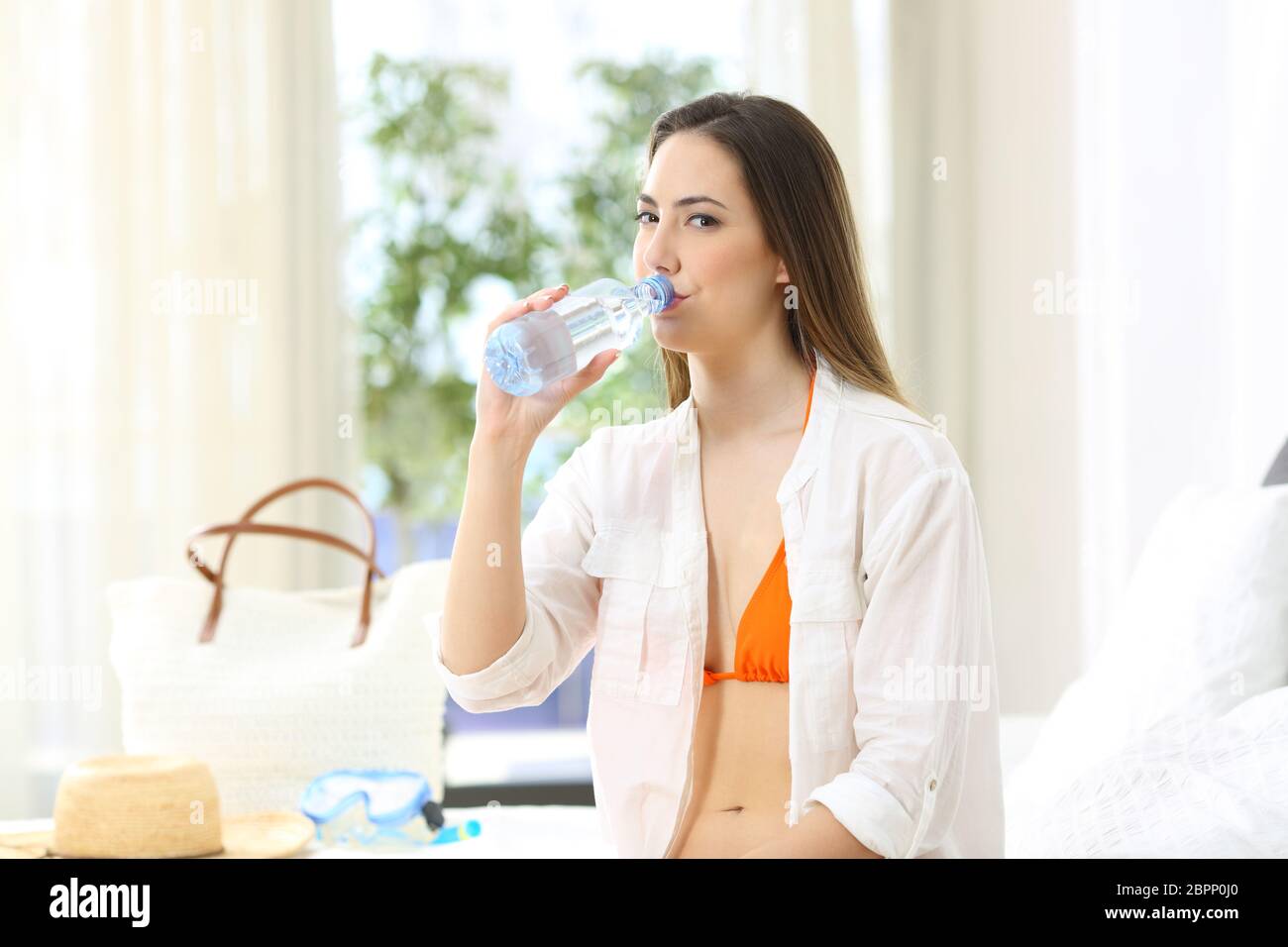 Relaxed tourist drinking bottled water in an hotel room during a travel