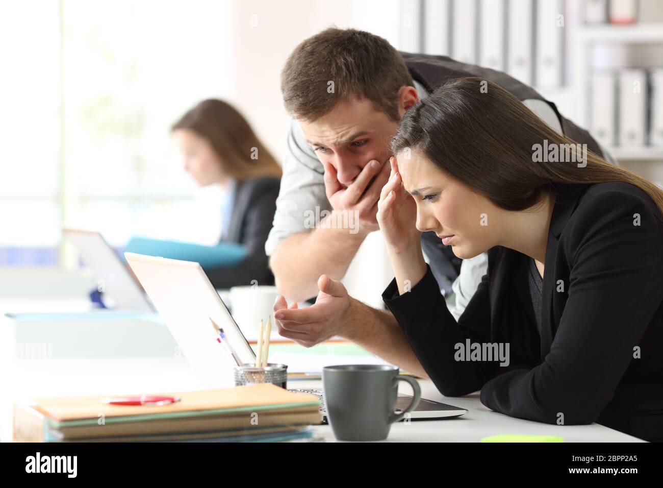 Two worried office workers checking online content in a laptop Stock Photo