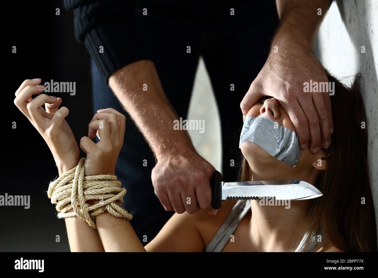 Terrified kidnapped woman being threatened by a kidnapper putting a knife in her neck indoors Stock Photo