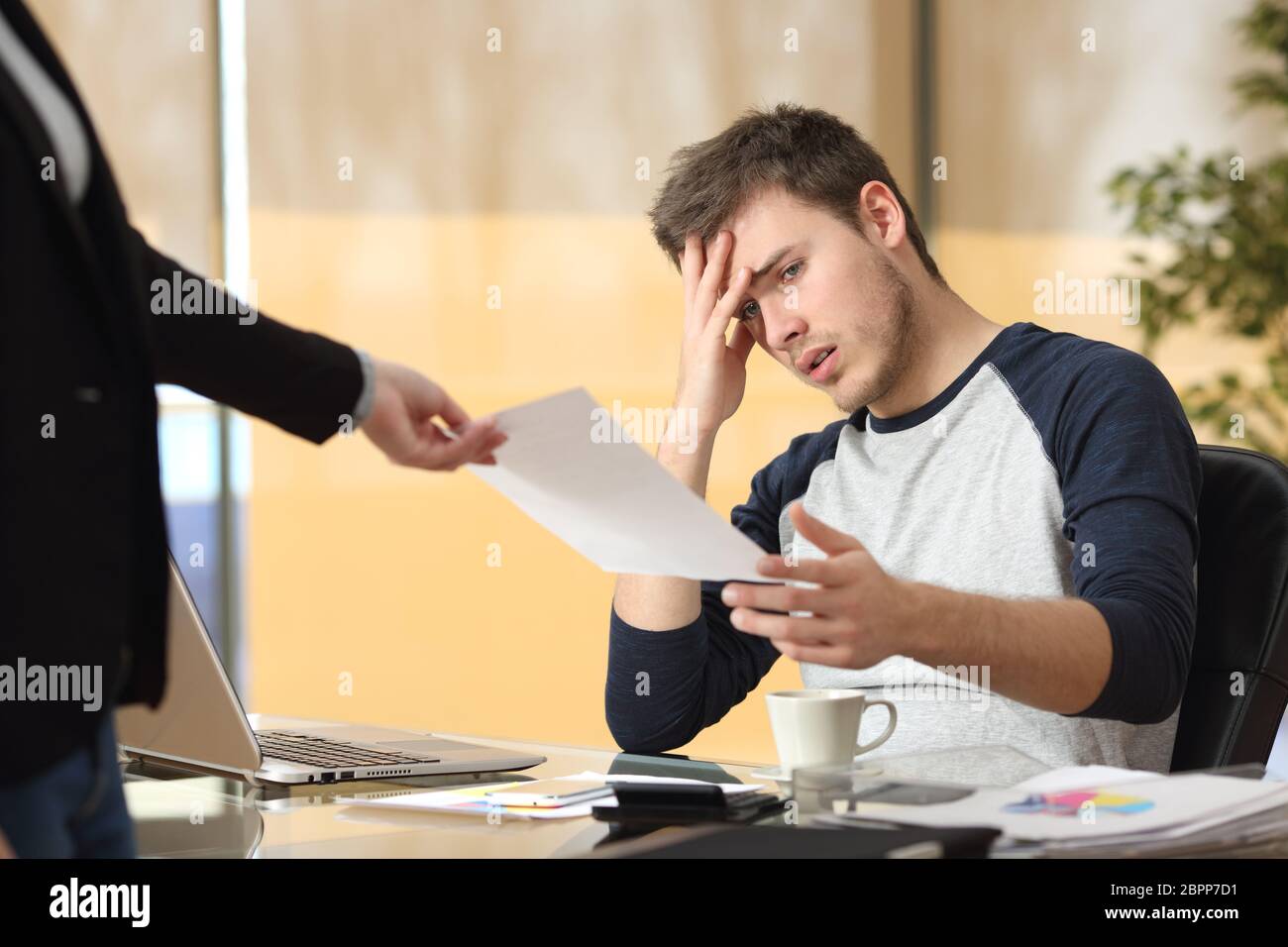 Worried intern receiving a dismiss notification or bad news from his boss or partner sitting in a desktop at office Stock Photo