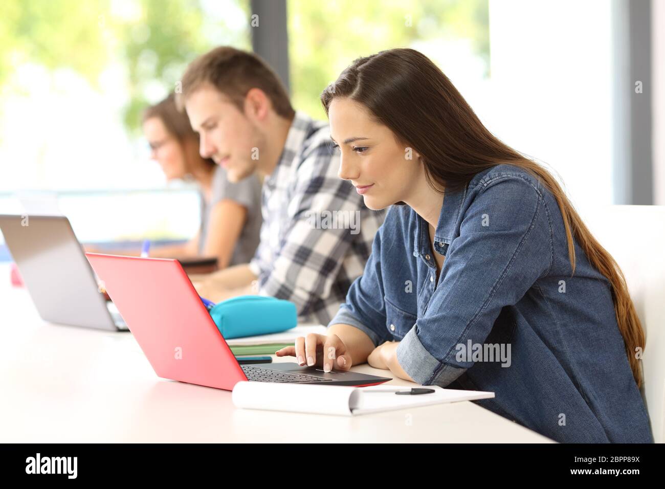 Side view of three attentive students e-learning on line with laptops ...