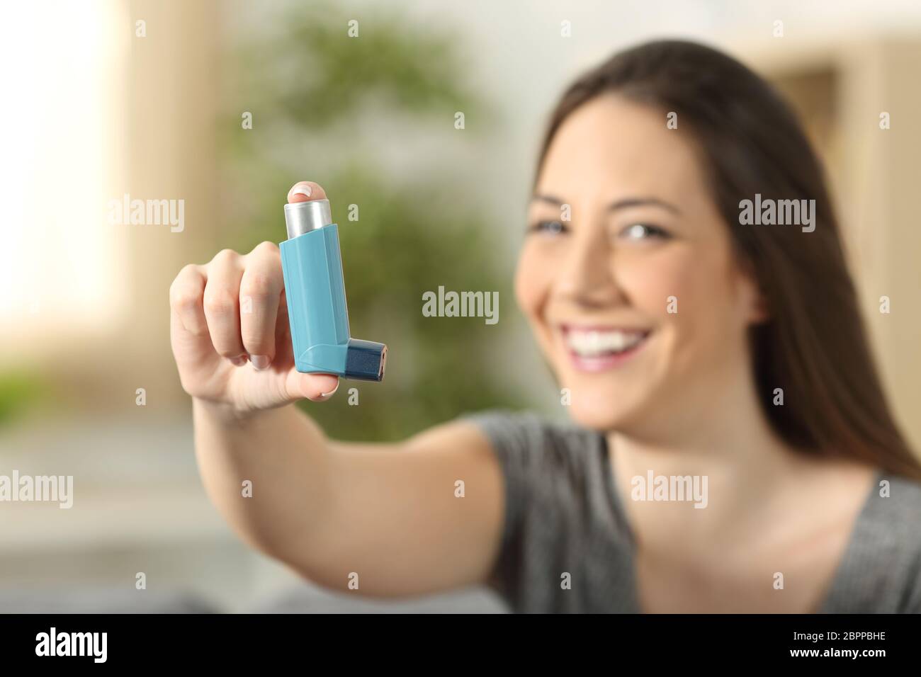 Girl showing an asthma inhaler sitting on a couch in the living room at ...