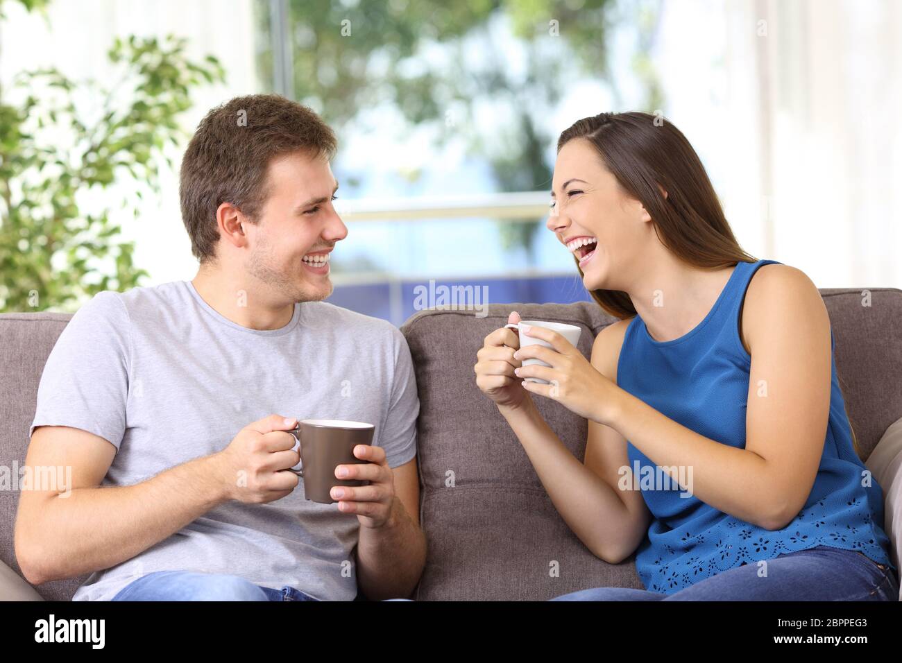 Two people talking and laughing loud sitting on a sofa at home Stock Photo  - Alamy