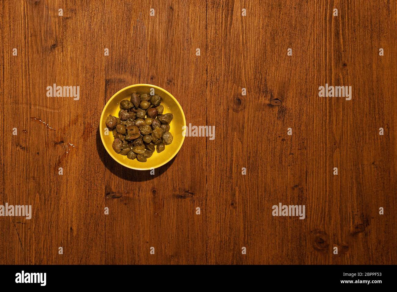 Top view of bowl full of capers on wooden background Stock Photo