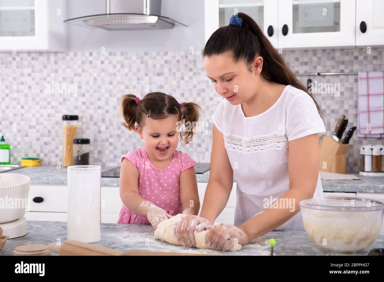 Happy Daughter Helping Her Mother Kneading Dough On Kitchen Counter ...