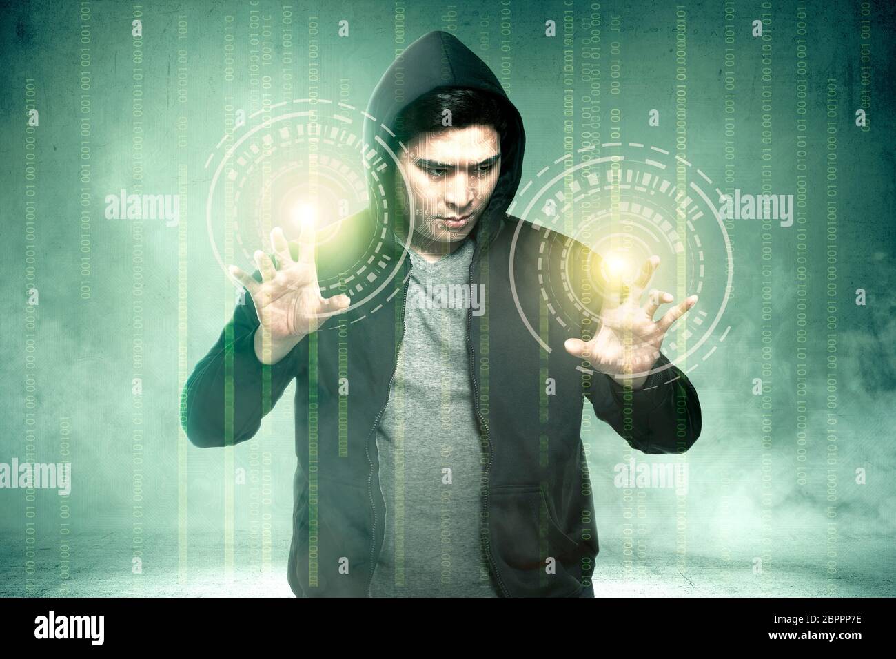 Young asian hacker in black hoodie touching virtual screen with binary code over green background Stock Photo