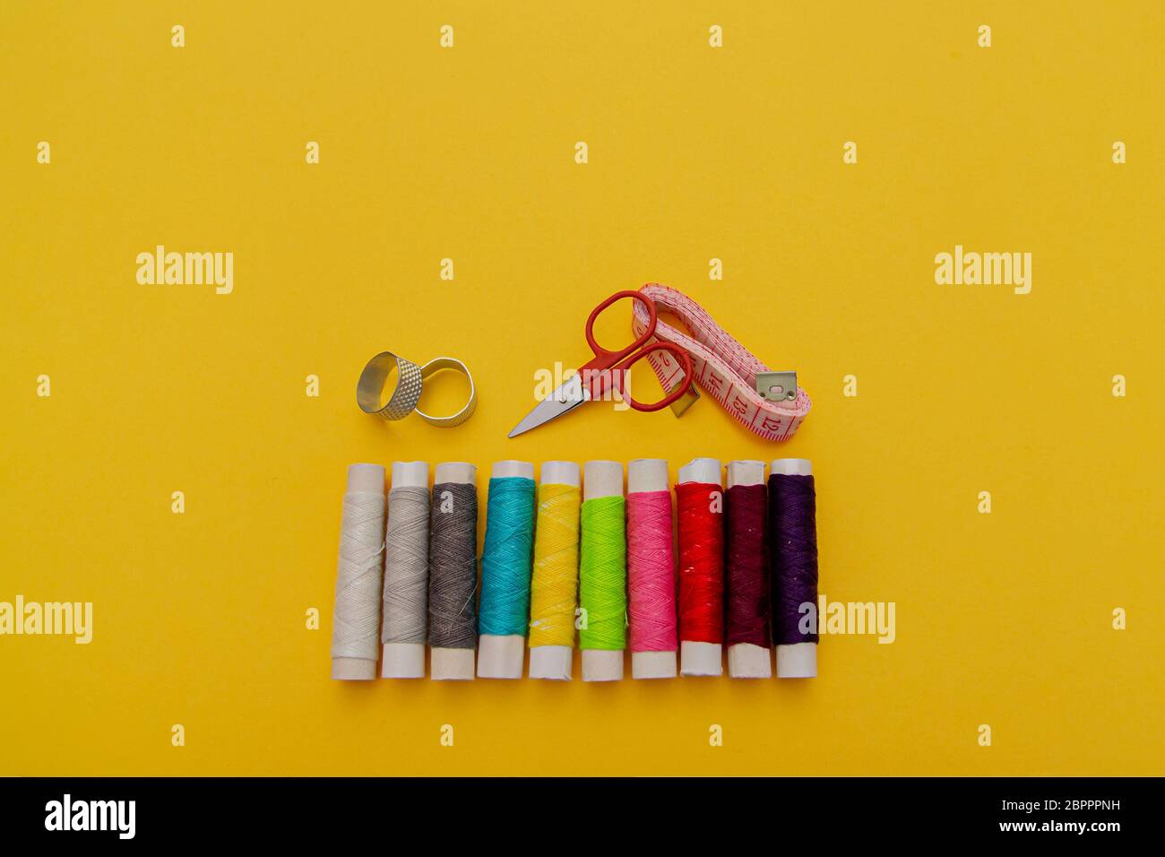Thread, needles, scissors and meter on yellow background. tailoring set. sewing kit multi-colored Stock Photo