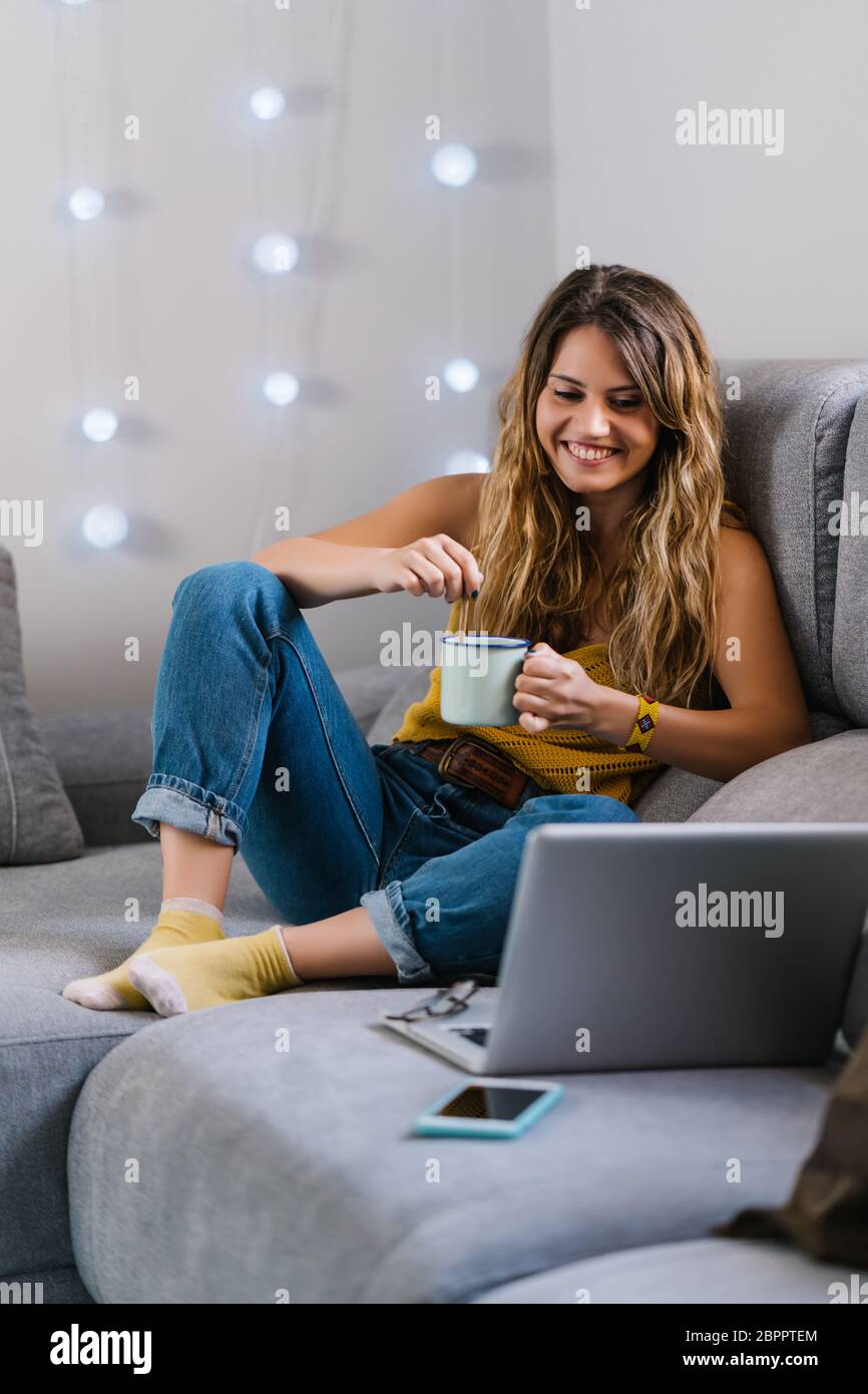 Woman sitting on sofa using laptop and drinking coffee Stock Photo - Alamy