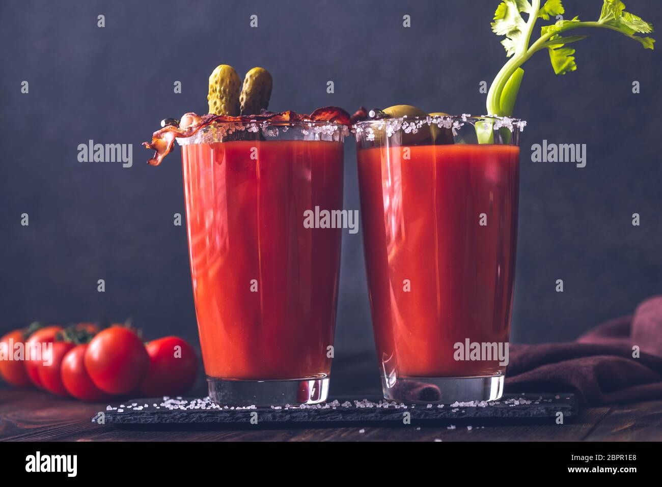 Two glasses of Bloody Mary garnished with gherkins, fried bacon strips