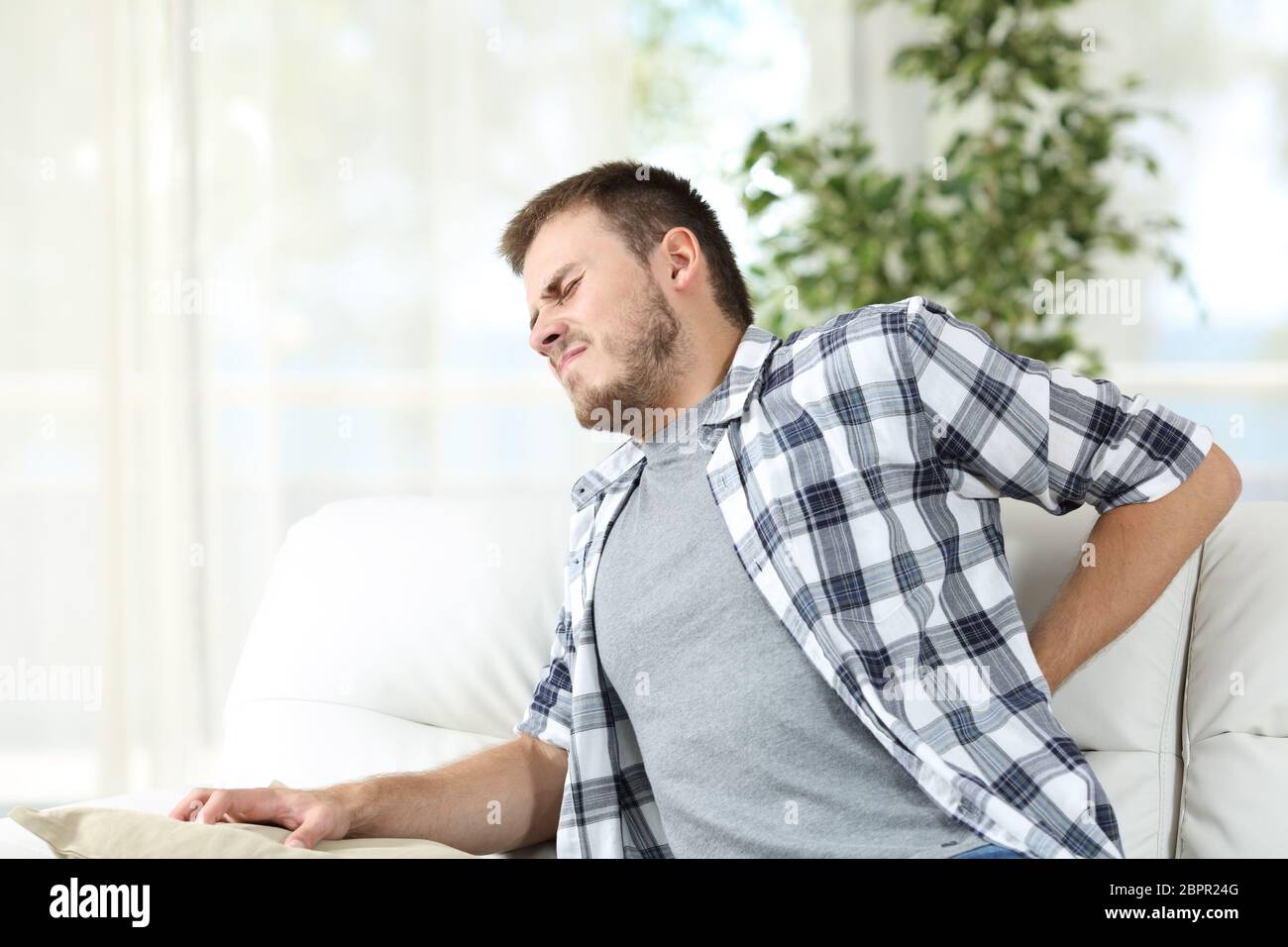 Unhappy man suffering back pain sitting on a sofa in the living room at