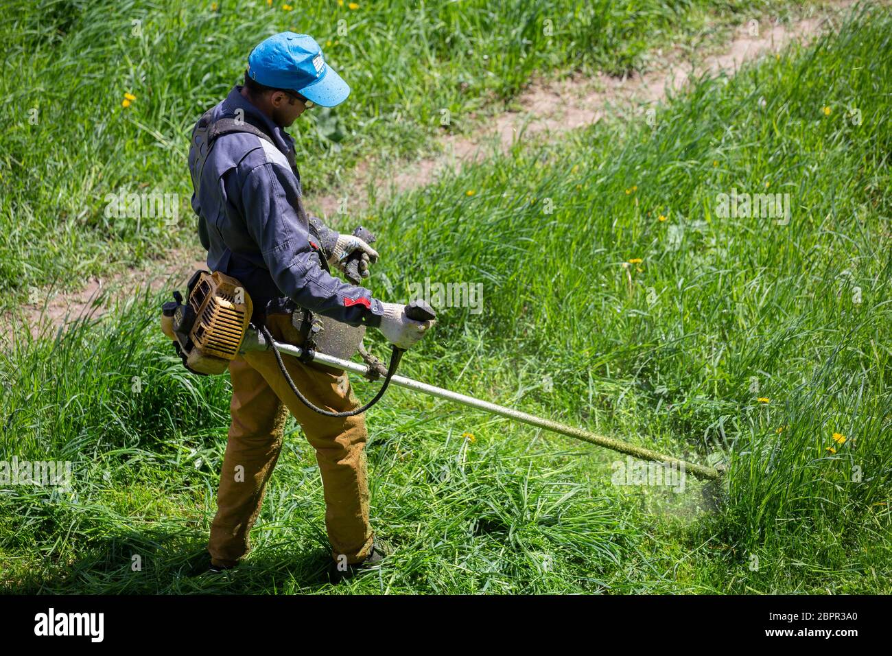 TULA, RUSSIA - MAY 19, 2020: Russian official lawnmower worker man cutting green grass with two-cycle engine string trimmer. Top to down view. Stock Photo