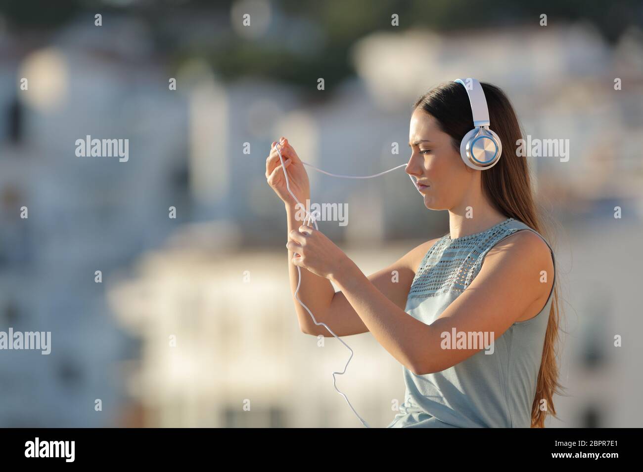 Frustrated woman fighting with the headphones cord in the street Stock Photo