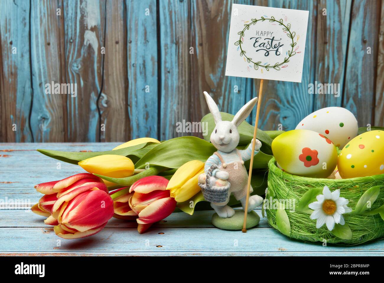 Colored easter eggs, easter rabbit and spring flowers on a wooden background with copy space. Greeting card, Easter background Stock Photo