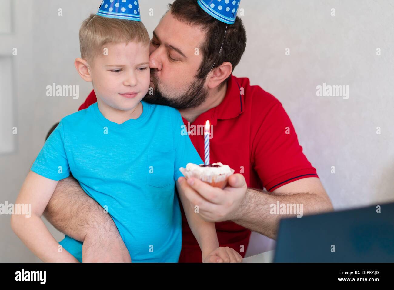 Little boy with his father celebrate birthday online, talking by notebook with relatives and friends. Blow out the candle on the cake Stock Photo