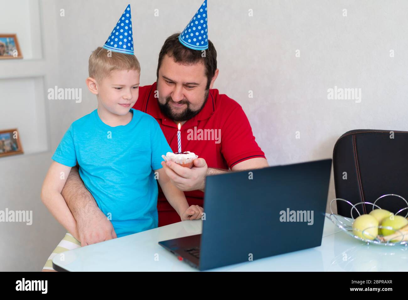 Little boy with his father celebrate birthday online, talking by notebook with relatives and friends. Blow out the candle on the cake Stock Photo
