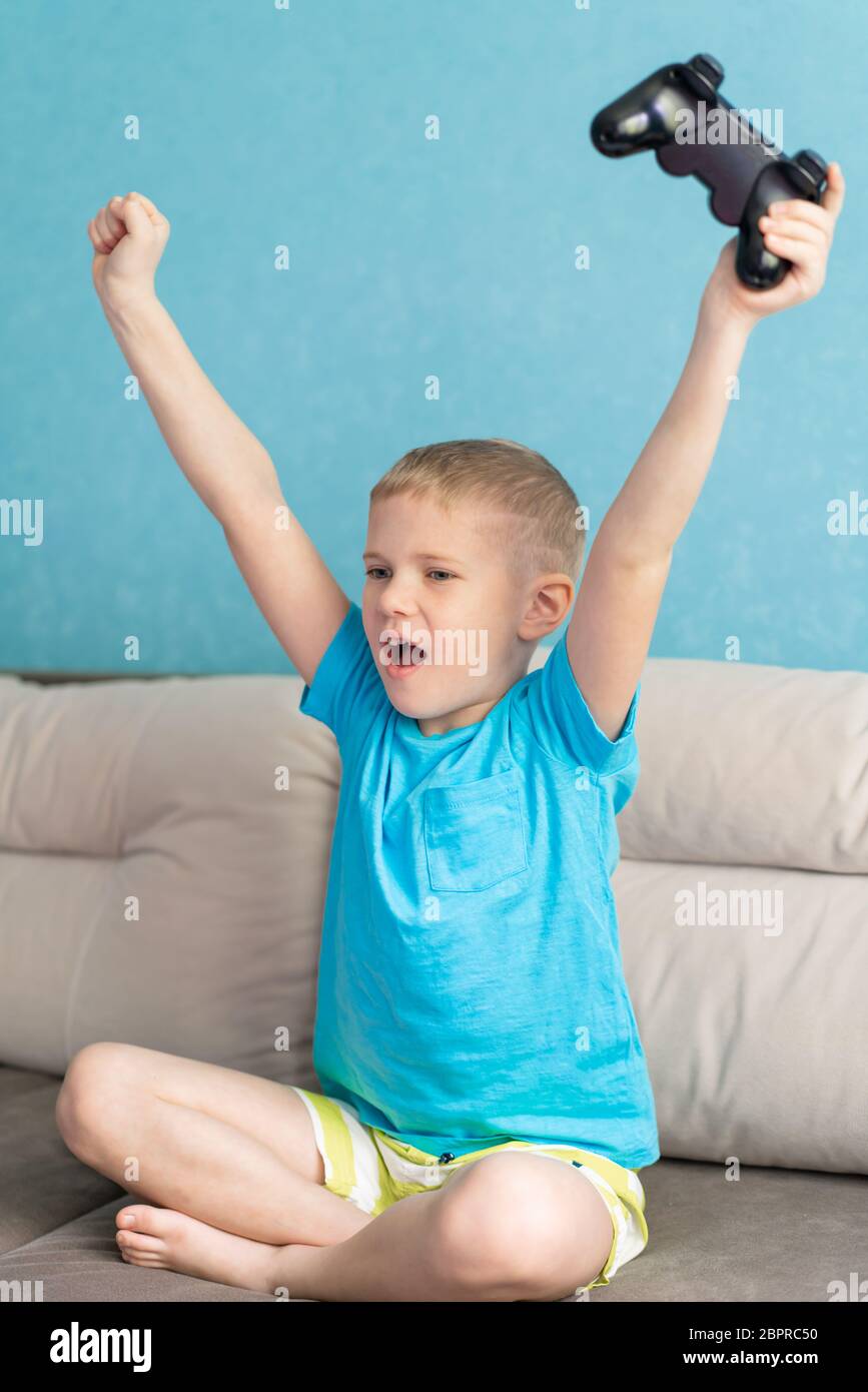 Little cute boy in blue t-shirt play with joystick in electronic game in his room Stock Photo